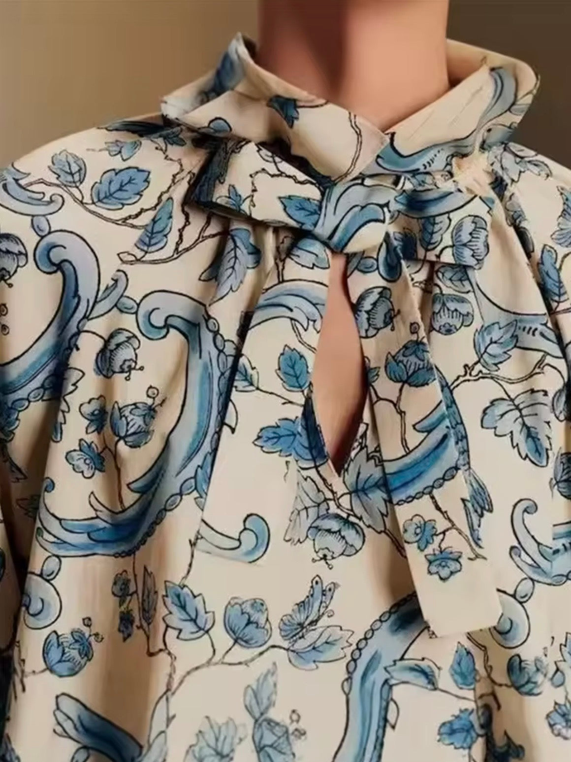 Camisa de cuello alto con estampado floral en color beige y azul claro y detalles de volantes