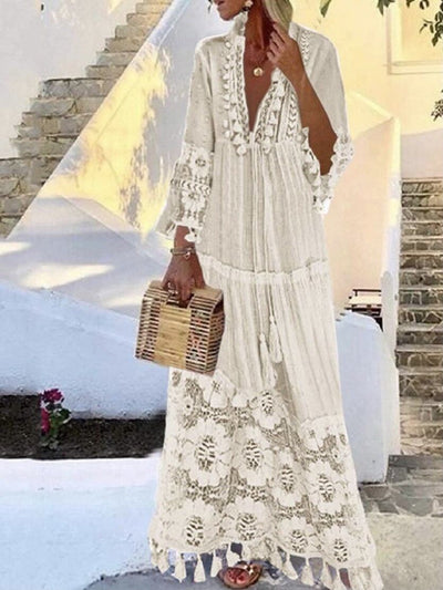 Model wears a white boho dress, mandarin collar, V-neck, long sleeves, drawstring at the front and tassel details accompanied by a boho bag